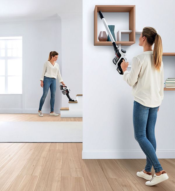 Woman vacuuming up dirt along the edge of the kitchen cabinet with the Unlimited.