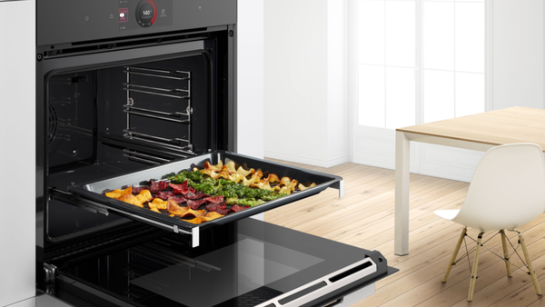 Bosch Einbau-Backofen mit Air Fry Funktion und herausgezogenem Backblech mit knusprig gebackenem Gem&uuml;sechips-Mix in moderner K&uuml;che.