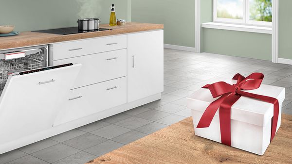 A gift tied with a red ribbon rests on a wooden countertop in bright, modern kitchen.