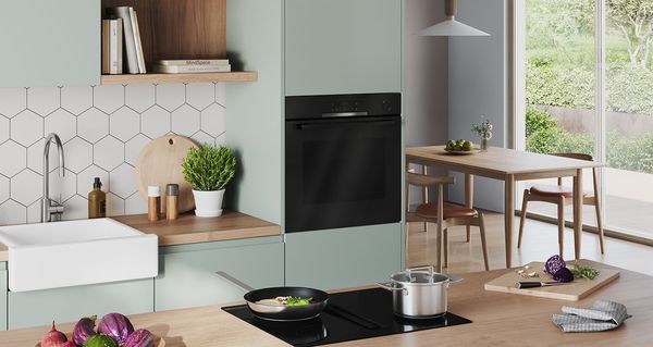 Una cocina luminosa y moderna, con una olla y una sartén en la placa y dos hornos al fondo.