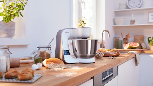 Eine weisse Küchenmaschine Serie 4 von Bosch steht in einer hellen Küche auf einer Holzablage.