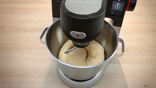 A mixer is actively blending ingredients to create a smooth dough in a kitchen setting.