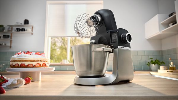 A blender sits on a kitchen counter beside a beautifully decorated cake, ready for culinary creations.