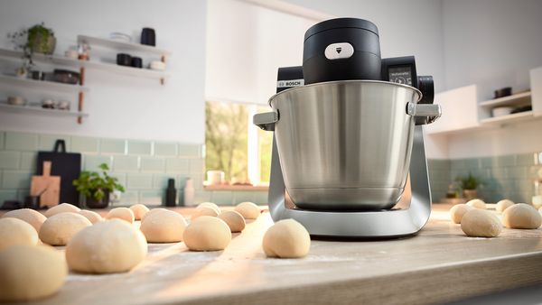 A mixer on a kitchen counter surrounded by neatly arranged dough balls ready for baking.