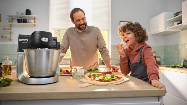 A man and a child joyfully prepare pizza together in a cozy kitchen, surrounded by ingredients and cooking tools.