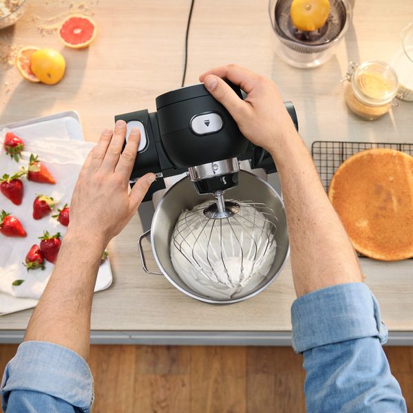 A person mixes strawberries with a hand mixer, highlighting the preparation of a fruit dish.