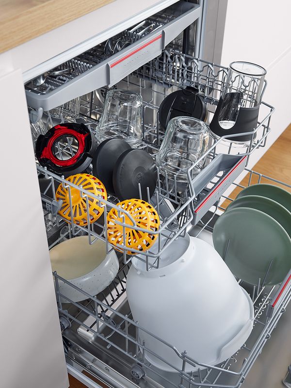 Dishwasher containing various stand mixer parts including plastic bowl, disc holders and jugs.