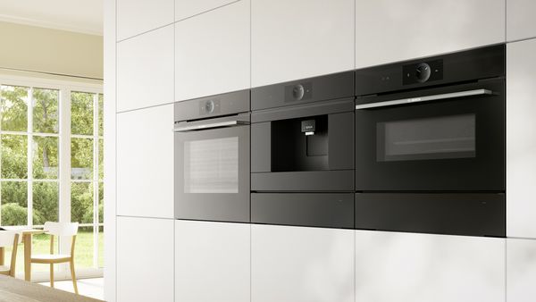 Built-in coffee machine next to built-in oven in a white interior kitchen.