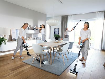 Young family vacuuming hard-to-reach spots in their living room with handheld cordless vacuums