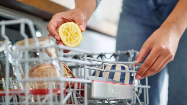 Frau gibt Zitrone in die Spülmaschine.