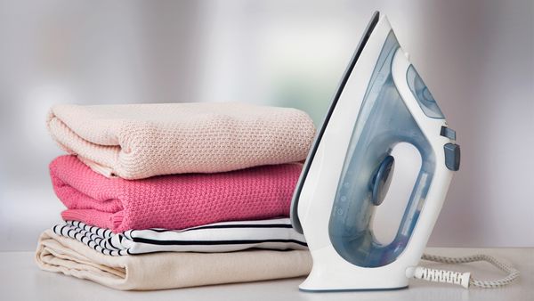 A neatly arranged stack of clothes beside an iron on a wooden table, ready for ironing and organization.