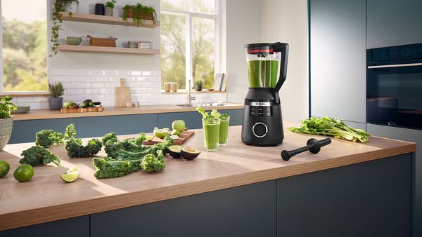 Auf der Arbeitsplatte einer Kücheninsel wird in einem Bosch VitaPower Serie 6 Standmixer ein zuckerarmer grüner Smoothie aus verschiedenen Obst- und Gemüstesorten zubereitet.