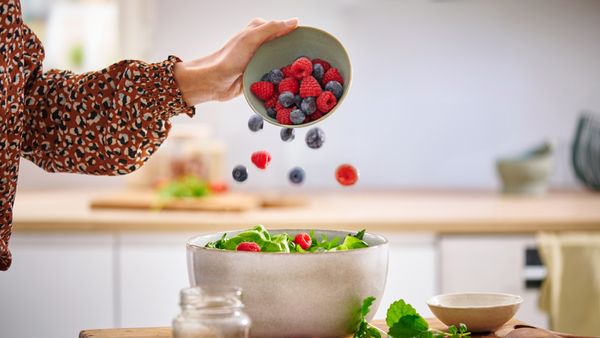 Model gibt Beeren zu einem Salat.