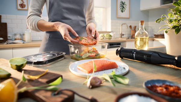 Eine Frau gibt Lachs mit Gewürzen für das Vakuumieren mit dem Bosch ErgoMaster Serie 4 in einen Spezialbehälter aus Glas.