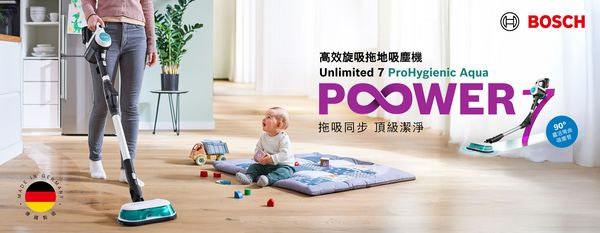 Young mother wipes the kitchen with the Unlimited 7 ProHygienic Aqua. Next to her a small child plays on a blanket with small toys on the wooden floor.