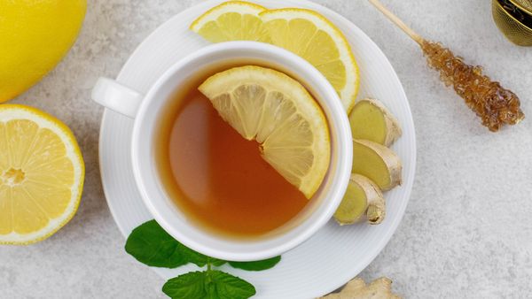  A steaming cup of tea garnished with fresh lemon slices and ginger, resting on a wooden table. 