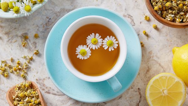 A cup of chamomile tea surrounded by chamomile flowers, highlighting its calming and health benefits.