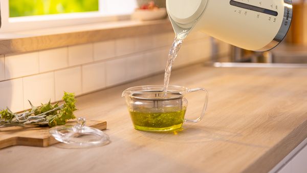 A person elegantly pours green tea from a teapot into a clear glass, showcasing the tea's vibrant color.