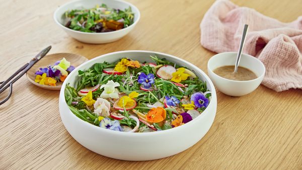 Eine Schüssel Salat mit essbaren Blüten auf einem Tisch.