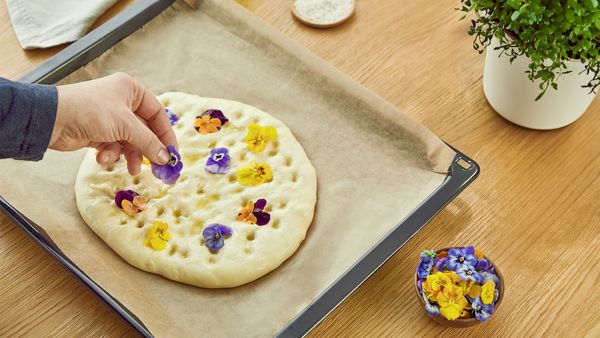 Ein Focaccia-Teig auf einem Backblech wird mit essbaren Blüten belegt.