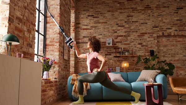 Eine Frau ist in einer weiten Schrittstellung tief nach vorne und saugt eine Fensterritze mit dem Bosch Unlimited 7 Akk-Staubsauger.