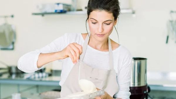 Chocolatière Sandra Serry-Eckhardt steht in einer Küche und verarbeitet weiße Schokolade in einer Schüssel mit einer Kelle.