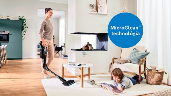 Na obrázku je moderná obývacia izba, kde osoba používa vysávač s technológiou MicroClean™. V miestnosti si dieťa pokojne prezerá časopis na podlahe. Tento scenár ukazuje kombináciu efektívneho upratovania a pohodlnej atmosféry pre rodinu.