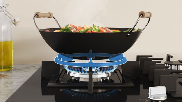 Un wok est posé sur la plaque de cuisson au gaz. Sous le wok se trouve un anneau de wok qui s'allume en bleu.