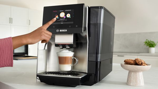 Η μηχανή καφέ Σειρά 8 με ένα χέρι που επιλέγει ‘cappuccino’ στην οθόνη αφής και από κάτω ένα φλιτζάνι cappuccino.
