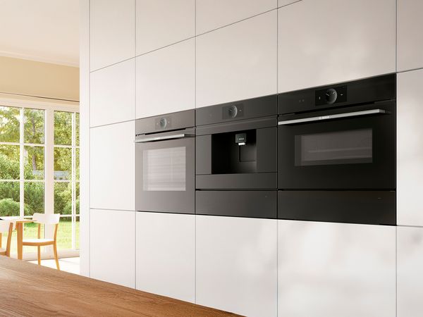 Aantrekkelijke inbouw Bosch oven en koffie volautomaat en magnetron in een lichte keuken.