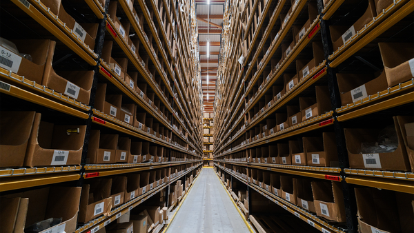 All&eacute;e d'un entrep&ocirc;t avec de hautes &eacute;tag&egrave;res remplies de cartons de pi&egrave;ces d&eacute;tach&eacute;es soigneusement rang&eacute;s.