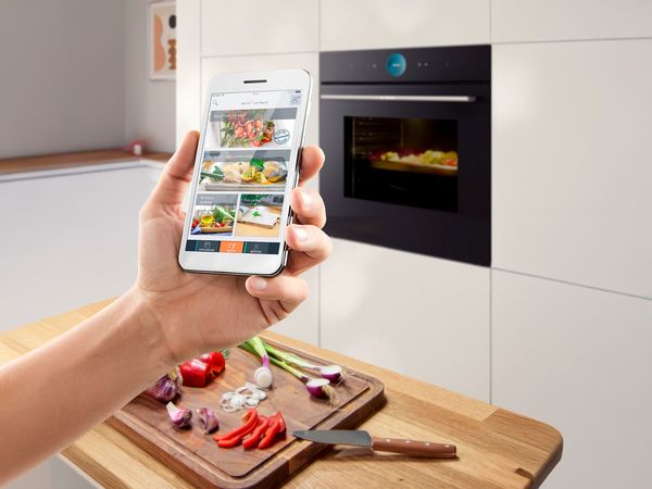 Smartphone con app Home Connect utilizzata per controllare da remoto un forno smart Bosch in cucina