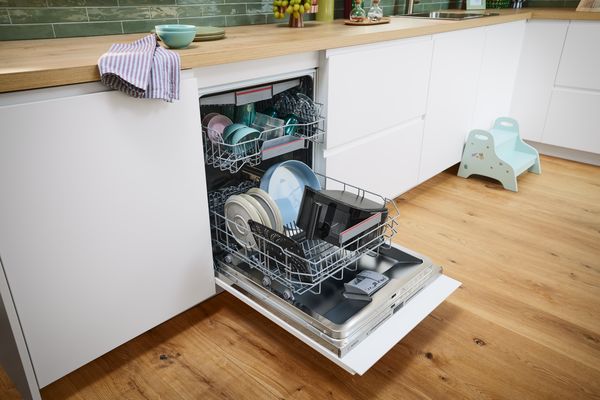 A woman rinses the basket of the Bosch Air Fryer under the sink faucet while the removable grid dries on a dish towel on the kitchen countertop.