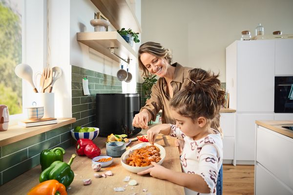 A young man slides a drawer filled with raw food into his Bosch Air Fryer, preparing for cooking in a bright kitchen.
