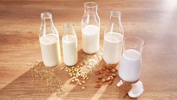 Various glass bottles with different types of milk: oat, soy, cow's milk, almond and coconut milk.