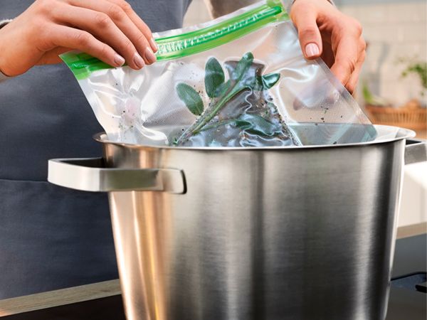 Mani che inseriscono un sacchetto con cibo sottovuoto in una pentola
