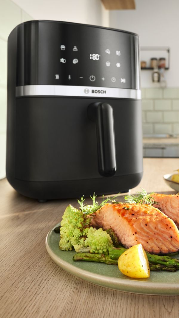 Air Fryer Serie 4 da Bosch com um prato de salmão cozinhado, legumes e molho colocado à sua frente.