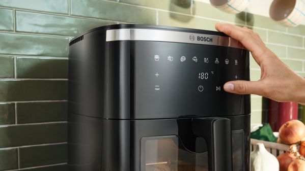 A mão de uma mulher a ajustar o painel de controlo da Air Fryer Bosch Serie 6 para definir o tempo de confeção.