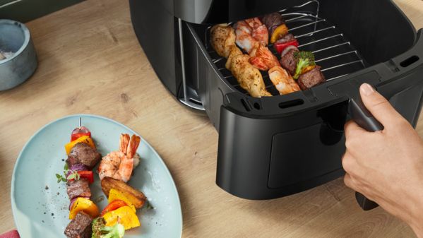 Um prato de espetos suculentos com bife grelhado, camarão e vegetais está ao lado da gaveta aberta de uma Air Fryer da Bosch.