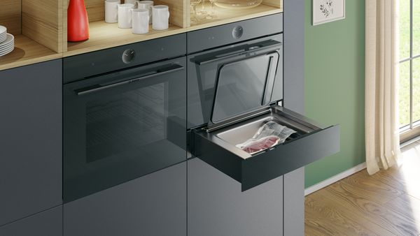 
       En åben sous-vide skuffe under en 45 cm ovn. En steak, der lige er vakuumpakket i en vakuumpose, er placeret i skuffen.
      