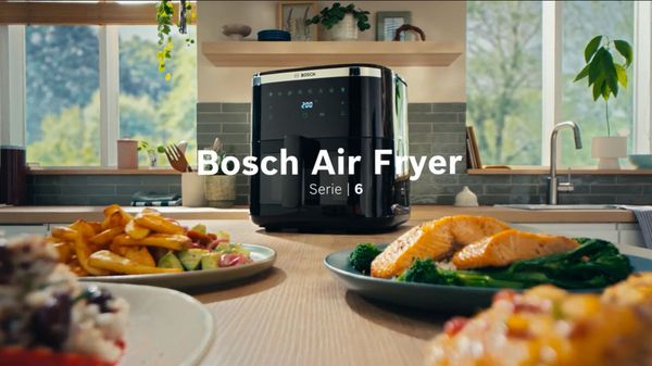Air Fryer Bosch Serie 6 com vários pratos, colocados numa bancada de madeira.