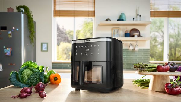 Uma Air Fryer Serie 6 está no balcão da cozinha rodeada de legumes frescos numa cozinha moderna e luminosa, pronta a cozinhar.