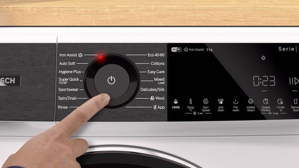 Una lavanderia con due lavatrici, vestiti appesi ordinatamente sopra, e scaffali con asciugamani piegati e contenitori per lo stoccaggio. Logo DITF visibile.