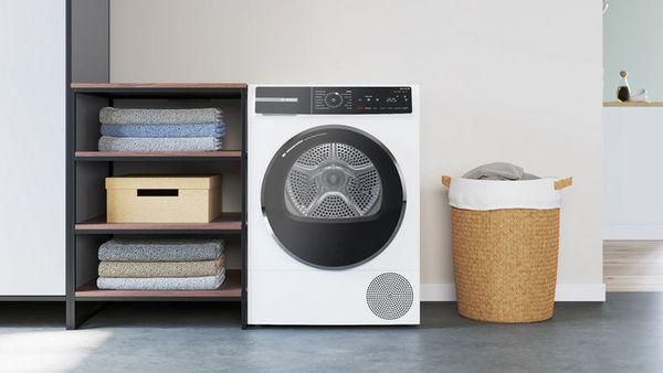 Lavanderia di casa con asciugatrice al centro, cesto portabiancheria e mobile con asciugamani ai lati