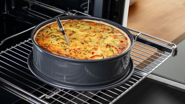 Brezžična sonda za meso, vstavljena v sredino velike pite v pekaču, ki stoji na izvlečeni rešetki pečice.