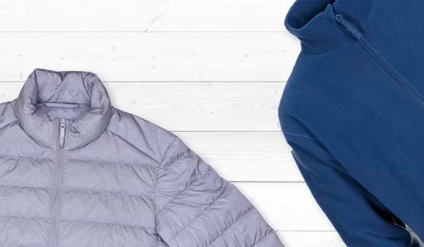 Eine graue Jacke und ein blauer Hoodie liegen auf einer wei&szlig;en Holzoberfl&auml;che.