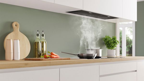 A modern kitchen with a wooden countertop, featuring a steaming pot, fresh herbs, and colorful vegetables.