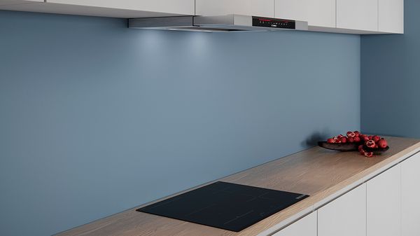 Moderne køkken med blå vægge, stilfuld emhætte, sort induktionskogeplade og en skål med røde frugter.