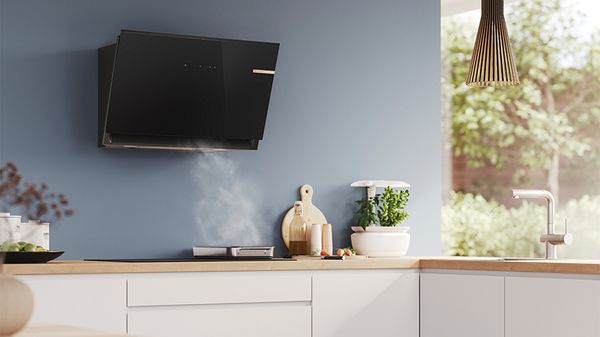 Modern kitchen with a sleek black wall-mounted range hood and steam rising from a pan.