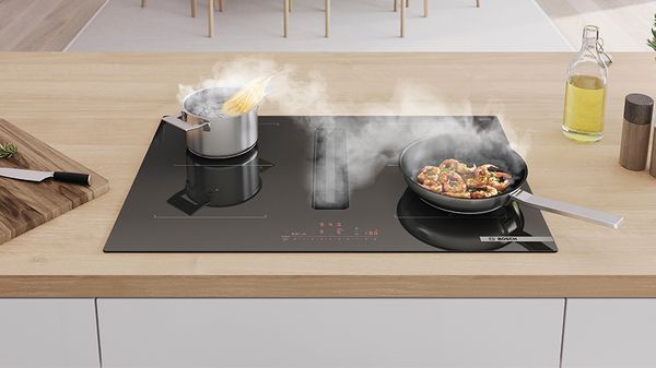 A modern kitchen countertop with a black induction cooktop, featuring aand a frying pan.